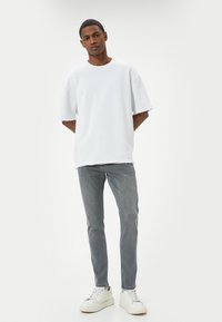 Biała, oversize'owa koszulka z surowymi brzegami, w połączeniu z jasnoszarymi, dopasowanymi dżinsami i białymi sneakersami. Prosty, minimalistyczny design.