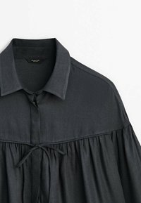 Zwarte stoffen shirt met een kraag met knopen, geplooide lijf met strikdetail en een gladde textuur.