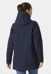 Parka impermeable de color azul marino con cuello alto, capucha ajustable y puños elásticos. Textura suave con corte recto y sin herrajes visibles.