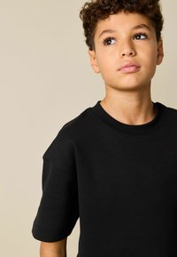 Camiseta negra de manga corta hecha de algodón, con un escote redondo y un ajuste relajado. Textura suave con detalles mínimos de costuras.