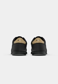 Black athletic shoes with a smooth textile upper, featuring a contrasting tan heel accent, and a textured rubber outsole.