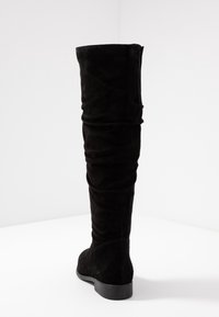 Czarne zamszowe kozaki do uda o luźnym kroju, płaskiej podeszwie i okrągłym nosku. Gładka faktura z delikatnym szwem wzdłuż szwu.