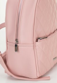 Prošívaný růžový kožený batoh se stříbrným zipem, boční kapsou a nastavitelnými popruhy. Hladký povrch s jemným leskem.