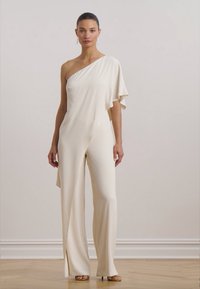 Kremast jumpsuit na jedno rame s lepršavim detaljem, širokim nogavicama i mekanim materijalom. Minimalistički dizajn bez vidljivih uzoraka.