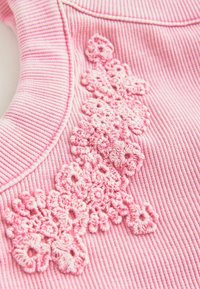 Pink ribbed textile with detailed floral embroidery in various shades of pink, featuring textured elements and a smooth neckline.