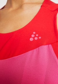 Gros plan d’une personne portant un haut de sport rouge et rose avec un groupe de six petits cercles roses en guise de logo sur la poitrine.