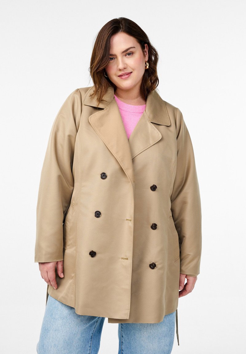 Trench coat beige con design doppiopetto, bottoni scuri, ampi risvolti e nastri laterali, realizzato in un materiale morbido e leggero.