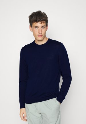 Navy blue long-sleeve sweater, crew neck, made of smooth fabric. Fitted design with ribbed cuffs, paired with light-colored trousers.