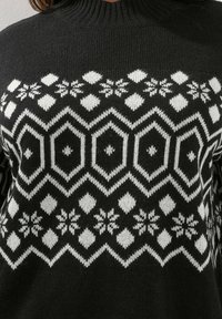 Suéter de punto negro con un patrón geométrico blanco que presenta hexágonos y copos de nieve. Diseño de cuello alto con textura acanalada.