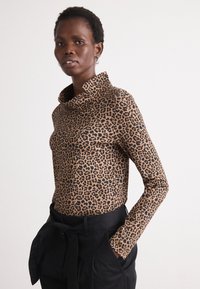 Leoparda raksta garām piedurknēm blūze bēšā un melnā krāsā ar nolokāmu apkakli. Saskaņota ar augsto jostasvietu melnajām biksēm un saistītu jostu.