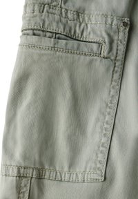 Hellgrüne Stoffshorts mit strukturiertem Finish, ausgestattet mit einer aufgesetzten Tasche und sichtbaren Nähdetails, einschließlich Metallnieten.