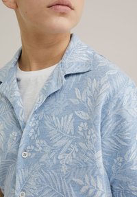 Camicia azzurro chiaro a maniche corte realizzata in tessuto testurizzato, con un sottile motivo floreale bianco e un colletto classico con due bottoni.