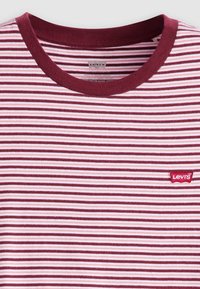 T-maica od pamuka u tamnocrvenim i ružičastim prugama s okruglim izrezom i malim crvenim Levi's logotipom na lijevoj strani prsnog koša. Mekana tekstura.