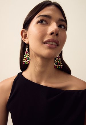 Woman wearing black top and gold Christmas tree earrings with red, green, and gold baubles, looking slightly upward and to the side.
