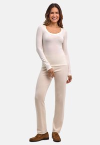 Kremowa bluzka z długim rękawem i okrągłym dekoltem, zestawiona z jasnobeżowymi obcisłymi spodniami; obie wykonane z miękkiego, elastycznego materiału. Dopełnieniem stroju są brązowe mokasyny.