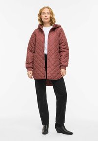 Vattert jakke med hette i en rosafarge, med trykknapper og sidelommer. Brukt over en hvit topp og svarte bukser med ankelstøvler.