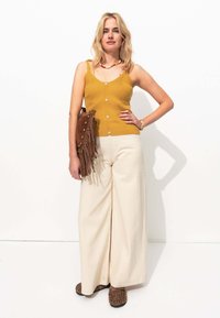 Débardeur en côtes moutarde avec des boutons sur le devant, associé à un pantalon large crème. Sac en suède frangé marron et chaussures à imprimé animal.