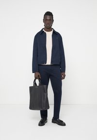 Marineblå jakke over lys cremefarvet sweater, parret med matchende marineblå bukser og sort læder tote bag. Sorte sko fuldender looket.