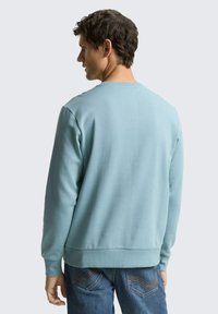Lichtblauwe sweatshirt met een ronde hals en geribbelde boorden. De stof oogt zacht en heeft een gladde textuur. Draagt een blauwe spijkerbroek.