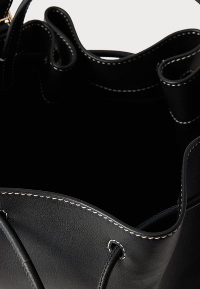 Sort læderbucket-taske med en glat tekstur, som har kontrasterende hvide syninger langs kanterne og en åben top.