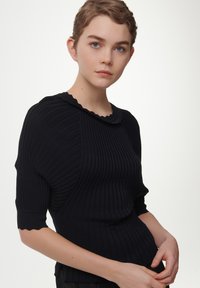 Suéter negro con cuello festoneado y mangas cortas. Tejido texturizado que exhibe líneas verticales y un diseño ajustado.