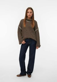Pull en tricot marron à manches larges, avec des bordures blanches. Associé à un jean large bleu marine et des chaussures marron. Coupe simple et décontractée.