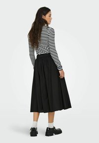 Gonna nera fino al ginocchio con vita arricciata, abbinata a una maglietta a maniche lunghe a righe bianche e nere. Modella che indossa scarpe nere con calzini bianchi.