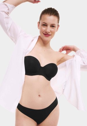 Zwarte strapless bh en bijpassende naadloze slip, beiden zonder naden. Model draagt een open wit shirt dat de soepele stof en het eenvoudige ontwerp toont.