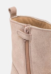Bota de ante hasta el tobillo en rosa claro con cierre de cremallera, con un forro de cuero suave y una pequeña lengüeta en la abertura.