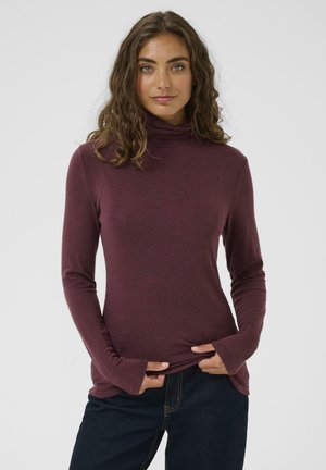 Burgundy long-sleeve turtleneck top with textured fabric, slim fit, and thumbhole cuffs, paired with dark jeans.