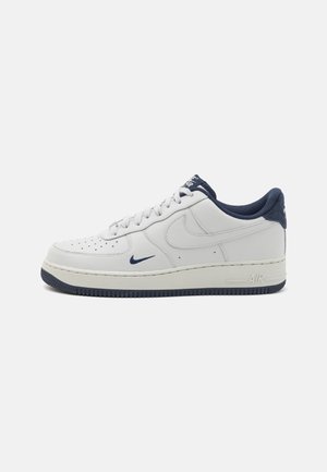 Sapatilhas Nike Air Force 1 de couro branco com detalhes em azul-marinho, bico perfurado, atacadores planos e sola de borracha texturizada.