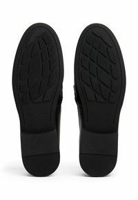 Suole di scarpe eleganti nere viste dal basso, con motivi geometrici sul battistrada e una leggera elevazione del tacco.