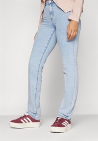 Ljusblå jeans med smal passform, med en slät yta och bakfickor. Matchas med burgundy sneakers med vita ränder.