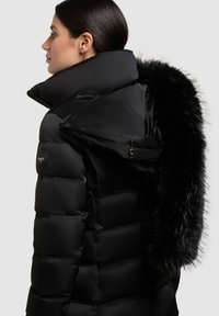 Mustast pufijakist, millel on kõrge krae, luksuslik must karvane ääreosa, tikkpind ja vasakul pool logoga detail.