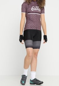 Kortärmad cykeltröja i mörkröd med vita detaljer, tillsammans med svarta shorts med en strukturerad grafisk mönster och grå cykelskor.