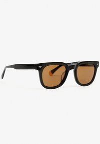 Gafas de sol negras de forma rectangular con lentes marrones, montura de plástico suave y un sutil detalle del logo en las varillas. Diseño clásico y minimalista.