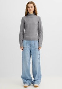 Suéter gris de punto con cuello alto y dobladillo acanalado, combinado con vaqueros cargo de pierna ancha en azul claro que cuentan con múltiples bolsillos y un diseño casual.