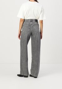 Väljettävät harmaat farkut, joissa on korkea vyötärö, kaksi takataskua ja ompeluyksityiskohtia, yhdistettyinä löysästi istuvaan valkoiseen t-paitaan.