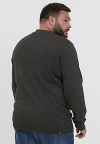 Pull en gris foncé à longues manches, avec des poignets et un ourlet côtelés, et un petit détail en étiquette marron en bas. Texture lisse, design simple.