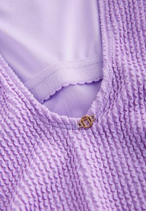 Laventelivärinen vaatekappale, jossa on tekstuurinen, rypytetty kangas, joka sisältää sileän sisävuoren ja kultasävyisen yksityiskohdan kaula-aukolta.