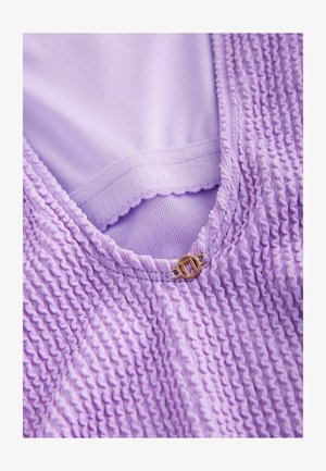 Laventelivärinen vaatekappale, jossa on tekstuurinen, rypytetty kangas, joka sisältää sileän sisävuoren ja kultasävyisen yksityiskohdan kaula-aukolta.