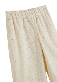 Pantalons beige clair en tissu texturé avec broderies florales et découpes. Taille élastique pour plus de confort.