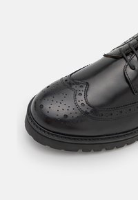 Zapato de vestir de cuero negro con detalles de brogue, punta redondeada y suela de goma resistente. Textura suave con perforaciones intrincadas.