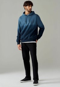Blauwe gradient hoodie met een trekkoord, met ribgebreide manchetten en zoom. Gecombineerd met zwarte broek en zwarte sneakers.