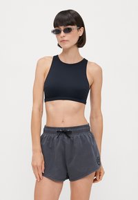 Top sportivo nero, pantaloni corti grigi con coulisse e logo, tessuto morbido, design aderente, top senza maniche, pantaloni corti con vestibilità comoda e fessure laterali.