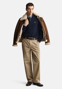 Rjava jakna z ovratnikom iz ovčjega krzna, mornarsko modra jopa, srajca z odporčastimi črtami, kaki hlače in temni čevlji. Opremljeno z zadrgo na ovratniku in vidnim pasom. Nevtralni toni.