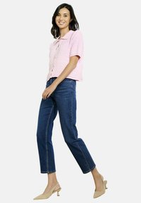 Hele roosa lühikeste varrukatega nööbiga särk tekstuurse kangaga. Kannab tumedate siniste sirgete pükste ja beežide säärelihasega kingadega.