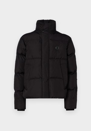 Juodas pūkinis švarkas su aukštu apykakle, turintis priekinį spaudimo uždarymą, dvi šonines kišenes ir mažą logotipą krūtinėje. Suruoštas tekstūra.