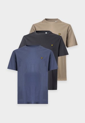 Hombre de pie con una camiseta azul de manga corta, pantalones cortos vaqueros claros hasta la rodilla, calcetines blancos y zapatos marrones con cordones.