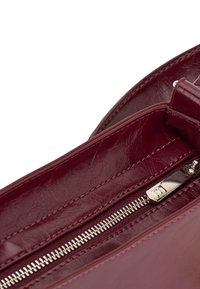 Burgundy bőr kézi táska cipzáras záródással, sima felülettel és belső zsebbel, ezüst színű fém részletekkel.